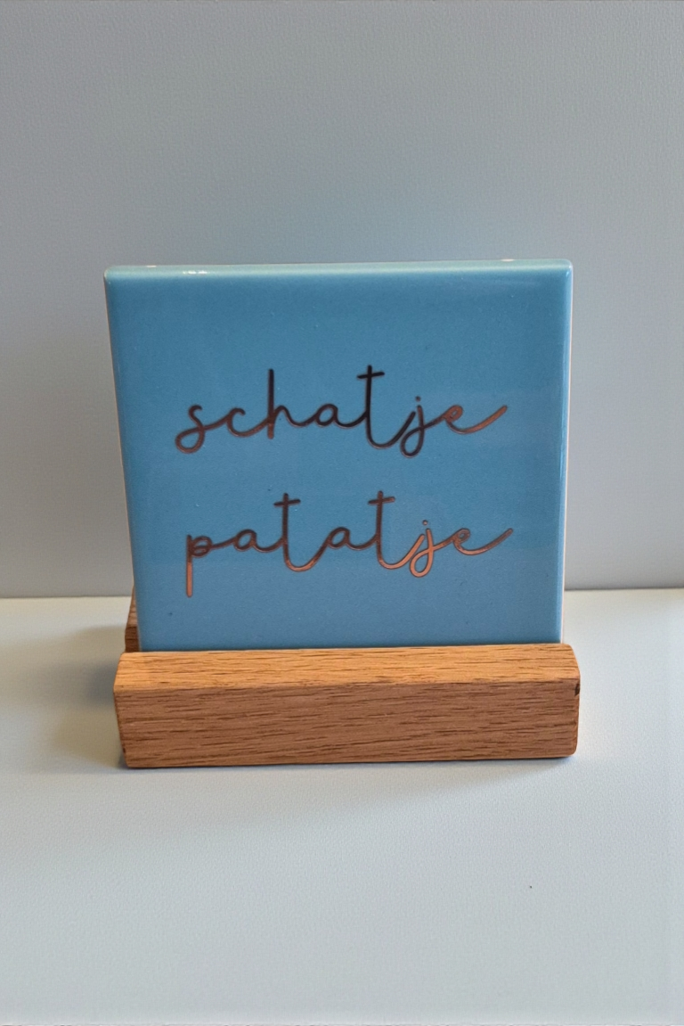Blauw tegeltje met rosé gouden tekst 'schatje patatje' in een houten houder.