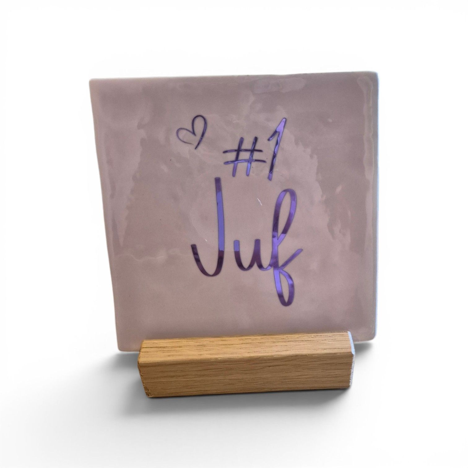 Drie tegeltjes met sierlijke letters, voor meester of juf, op een rustieke houten tafel tegen een witte muur.