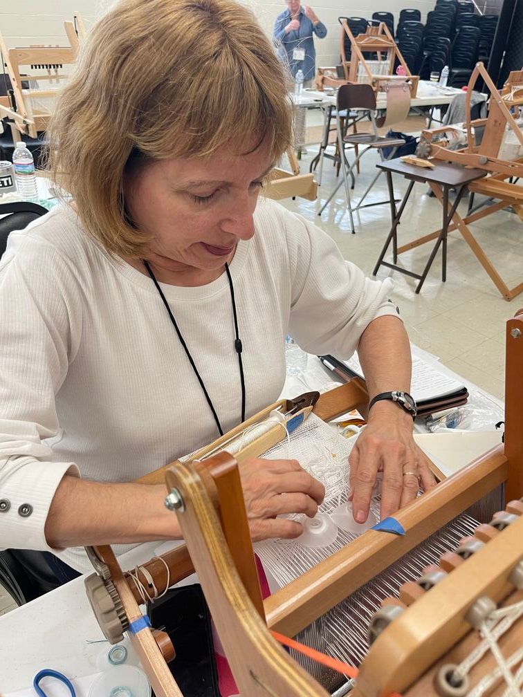 A fort worth weaver's guild member  sitting at a table working on a loom.
