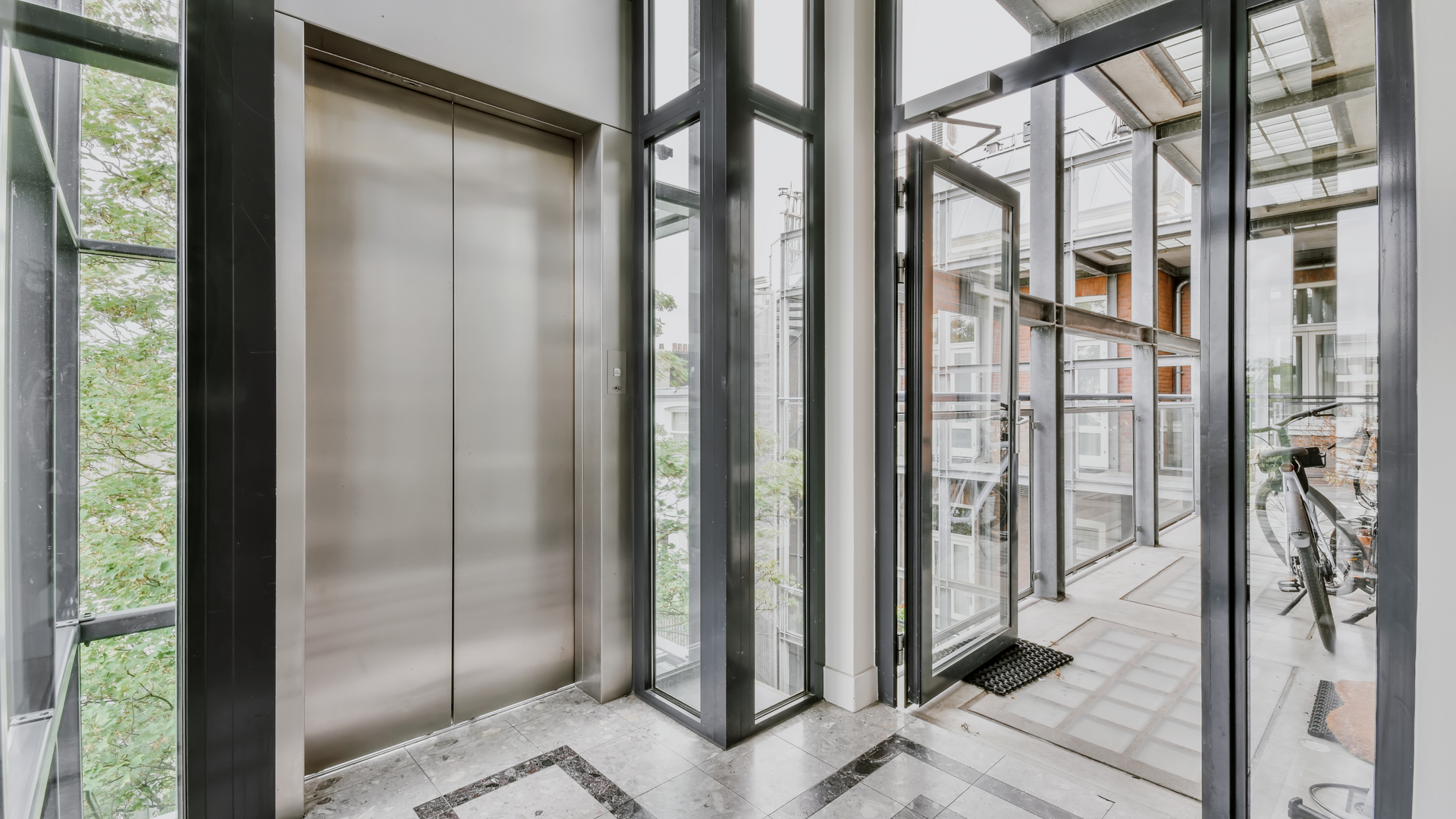 An elevator with a glass door and stairs in the background.