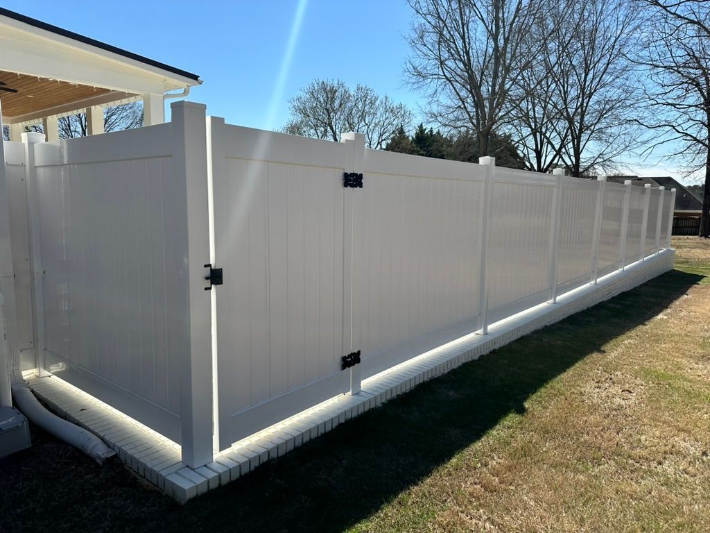 A white vinyl fence with a gate in the backyard of a house.