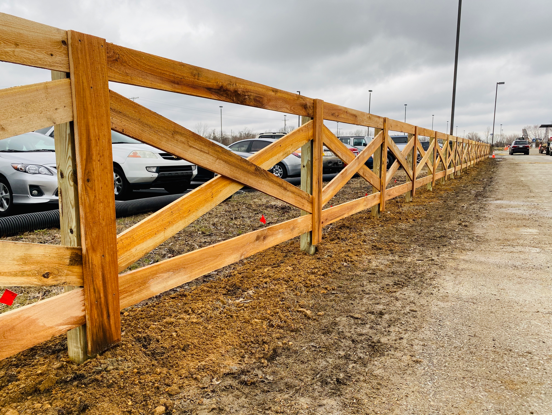 A wooden fence surrounds a parking lot with cars parked behind it.