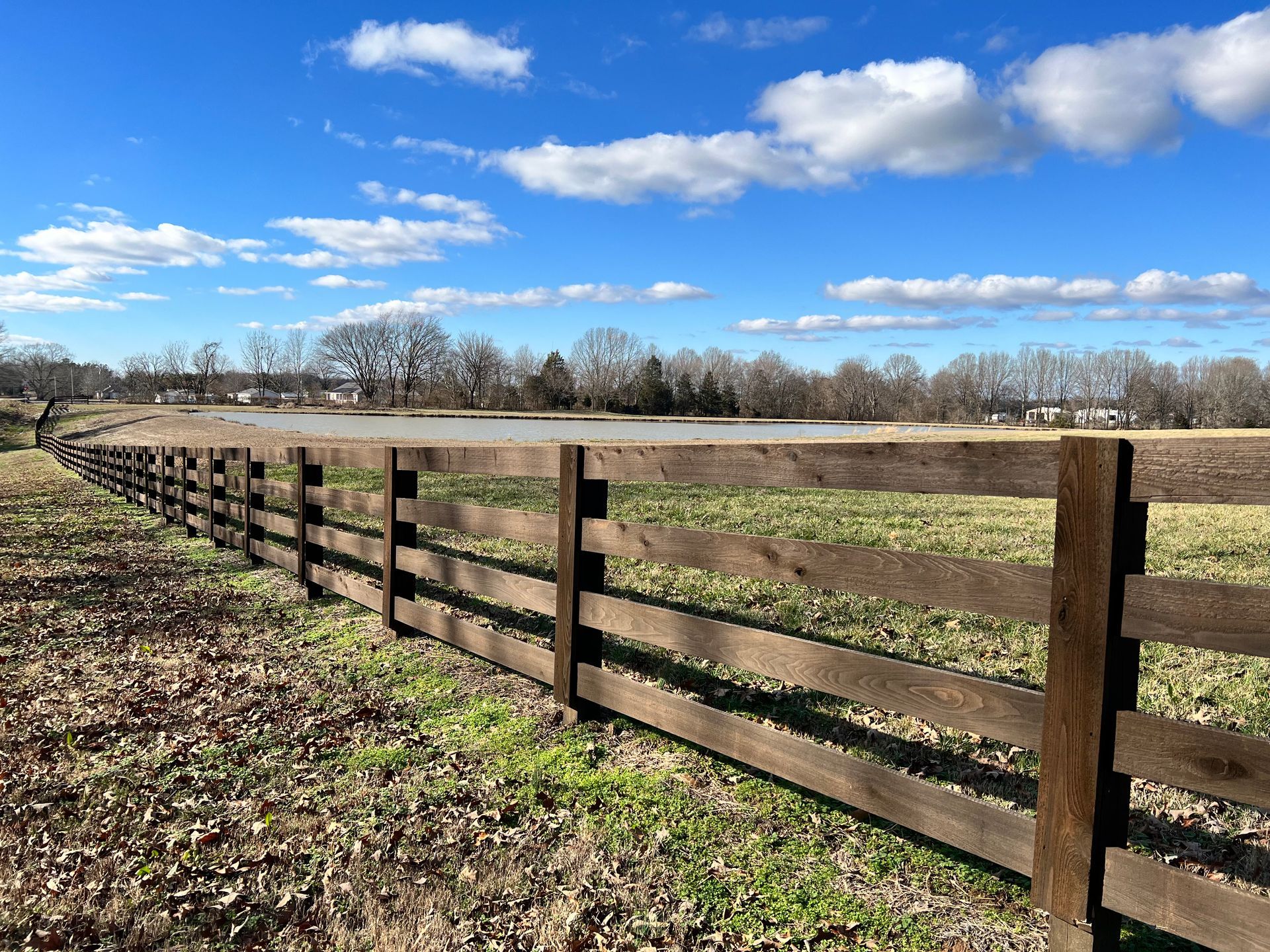 A wooden fence surrounds a grassy field on a sunny day.