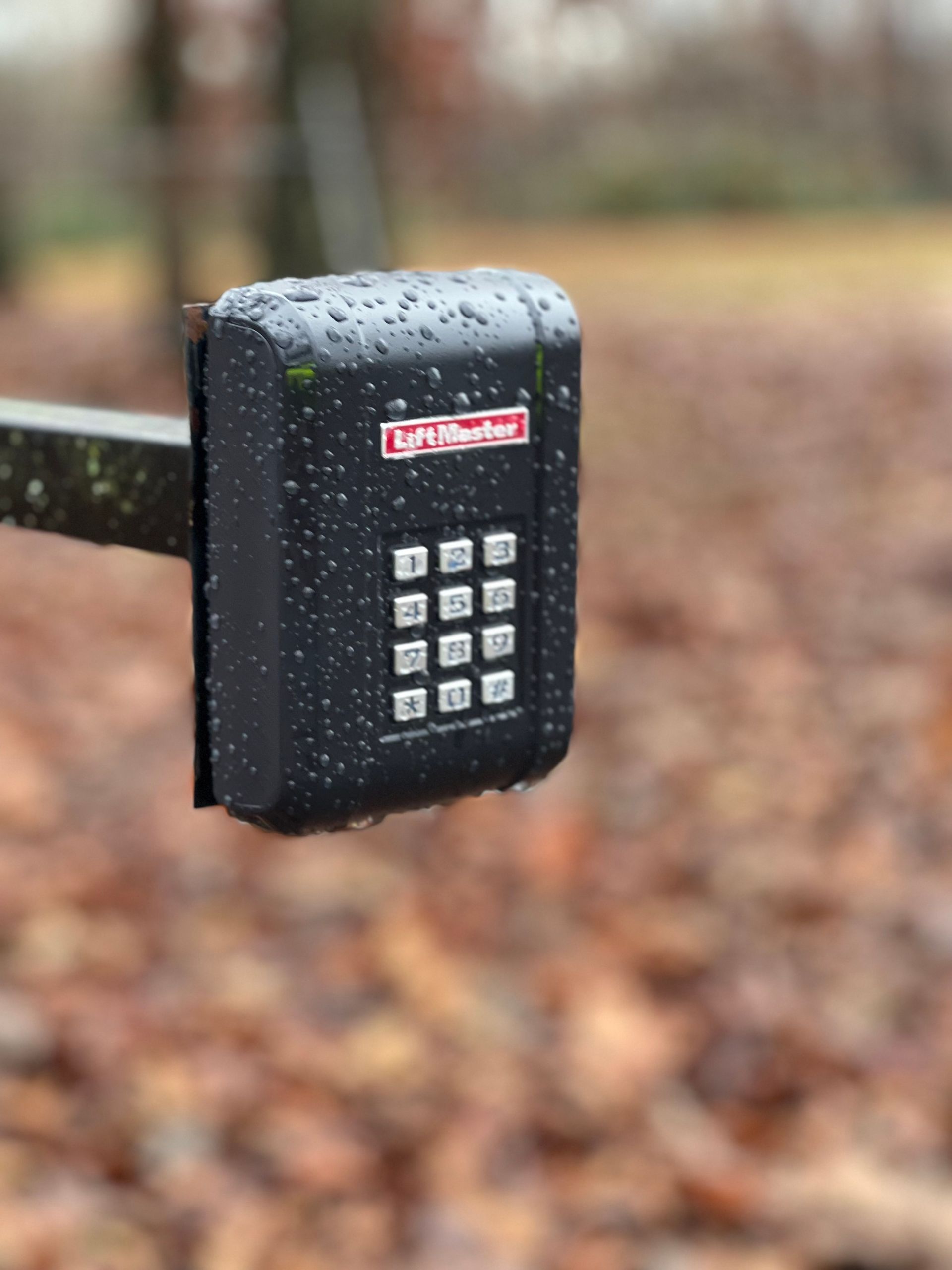 A close up of a keypad on a fence with leaves in the background.