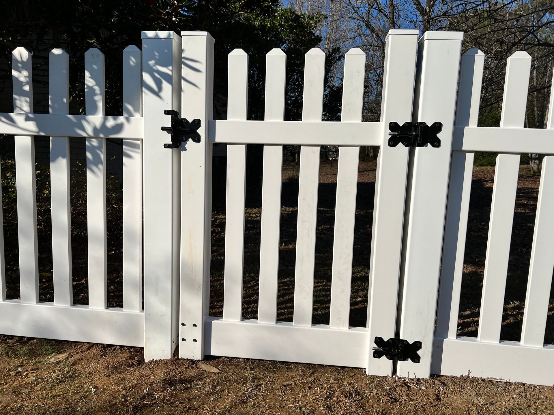 A white picket fence with black hinges is sitting on top of a dirt field.