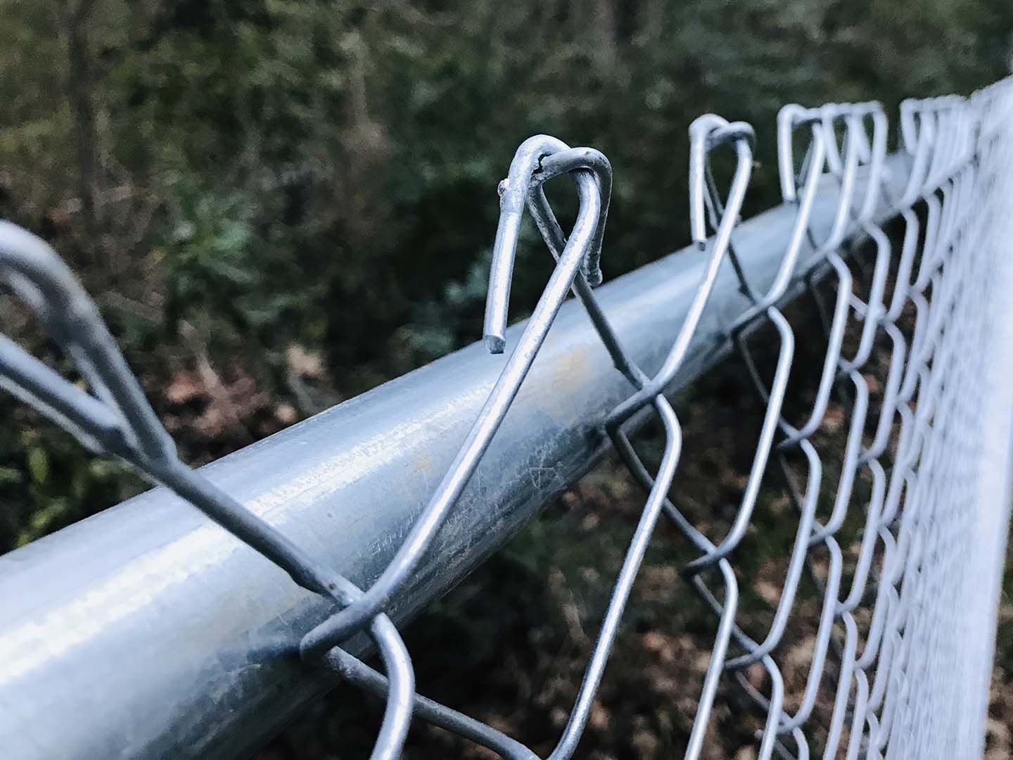 A close up of a chain link fence with trees in the background.