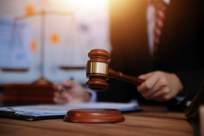 A judge holding a gavel at a desk with law documents and scales of justice in the background.