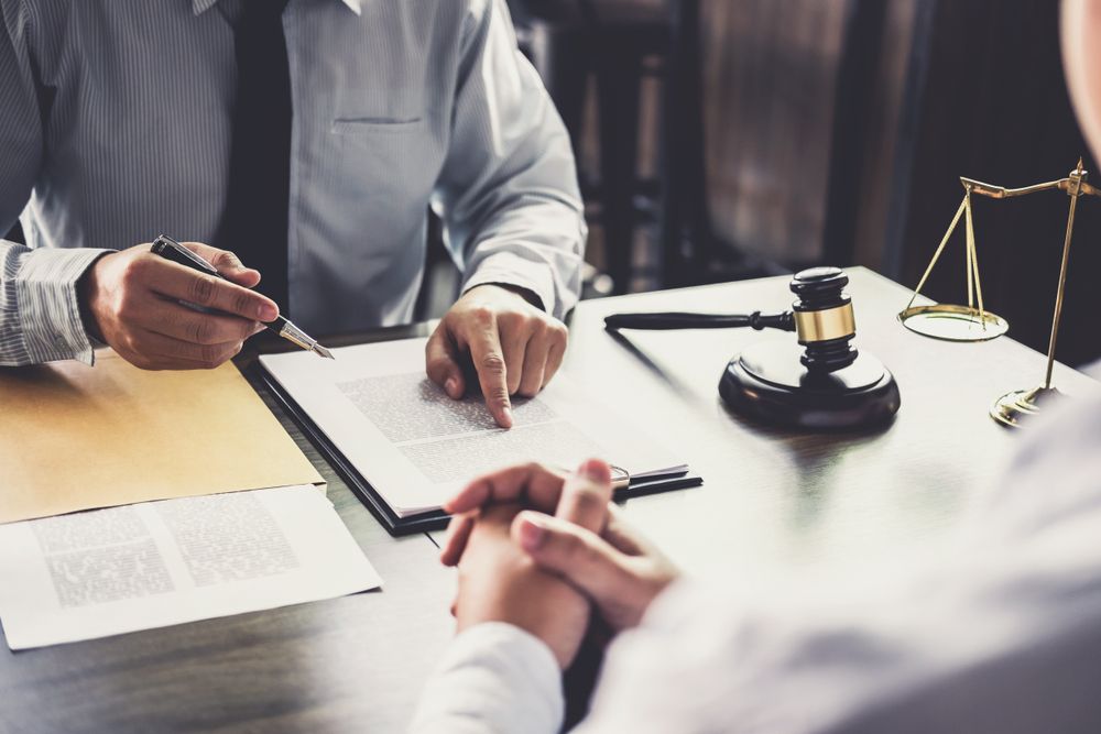 Lawyer pointing at document, reviewing with client; desk with gavel and scales in office.