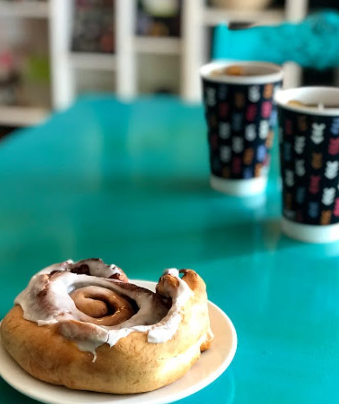 A cinnamon roll sits on a white plate on a blue table