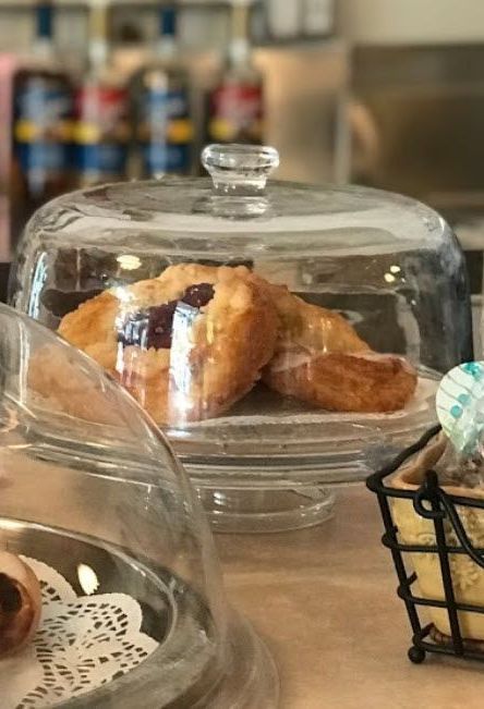 A glass cake stand filled with pastries and a basket of cupcakes on a table.