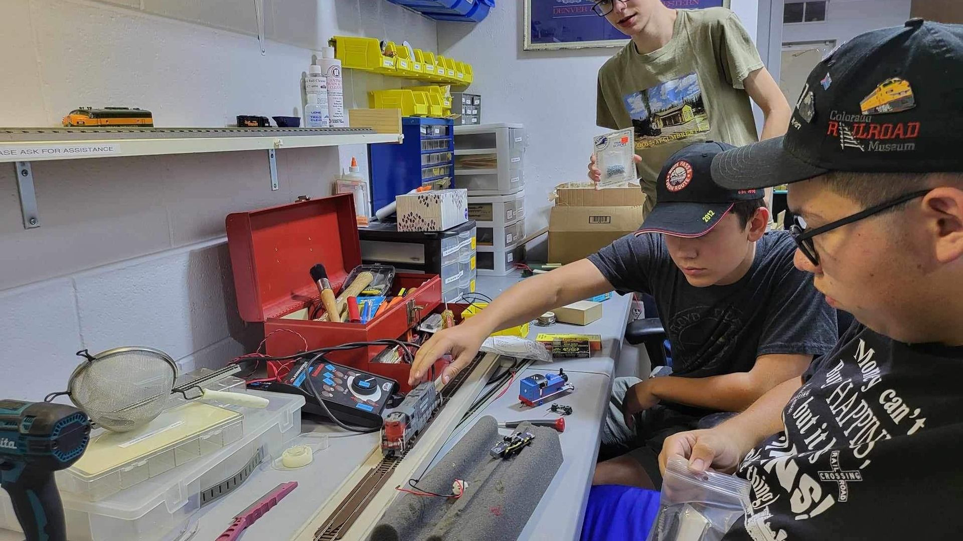 A group of men are working on a model train set in a workshop.