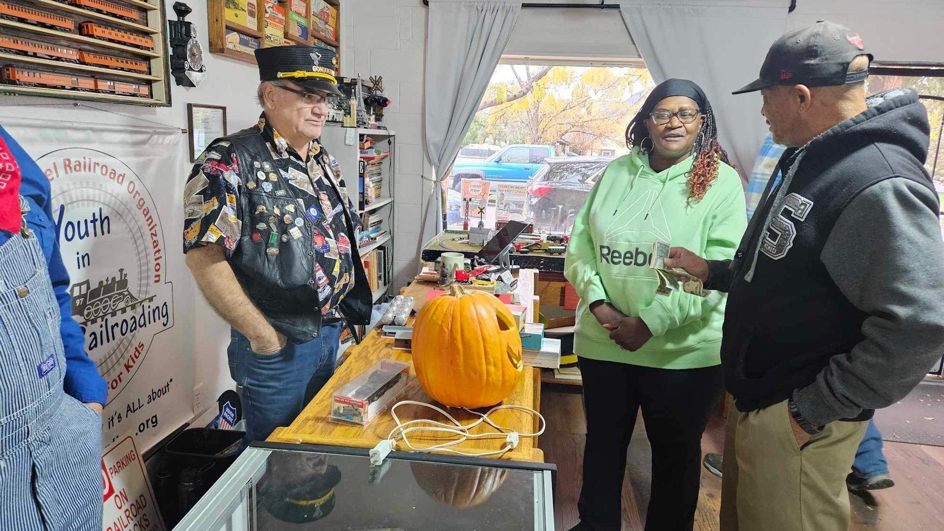 A group of people are standing around a table with a pumpkin on it.