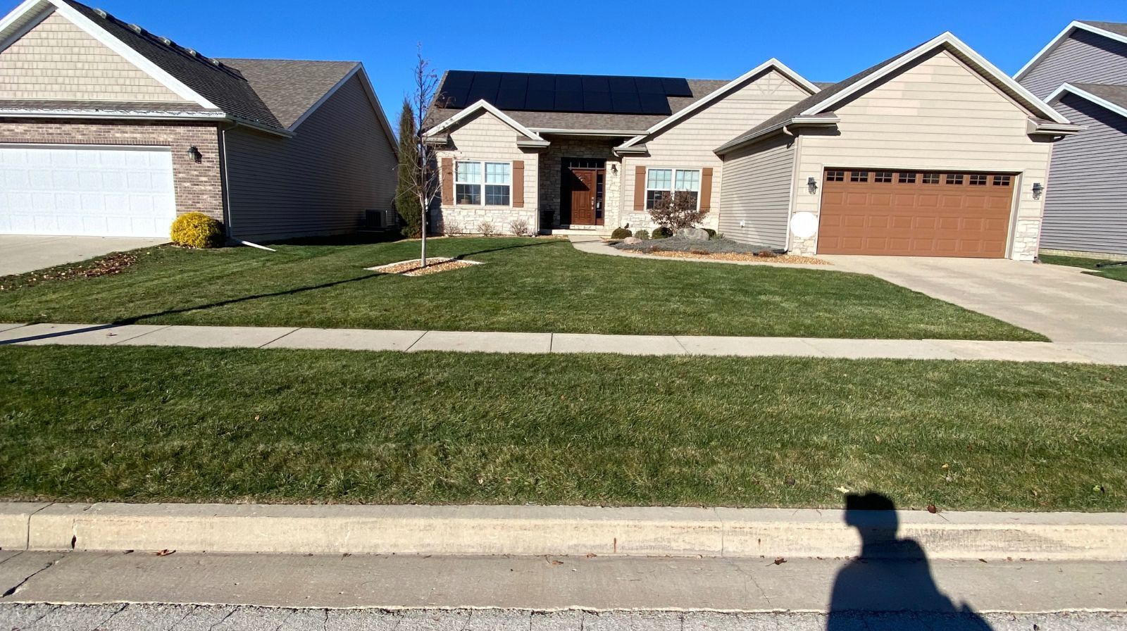 Houses with green lawns and blue sky. The house in the middle has solar panels on the roof.