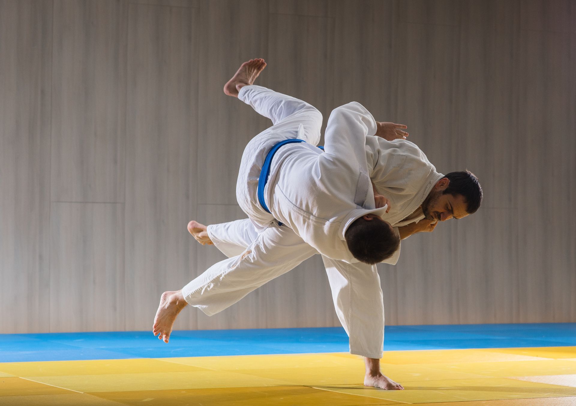Two men are practicing judo on a mat in a gym.