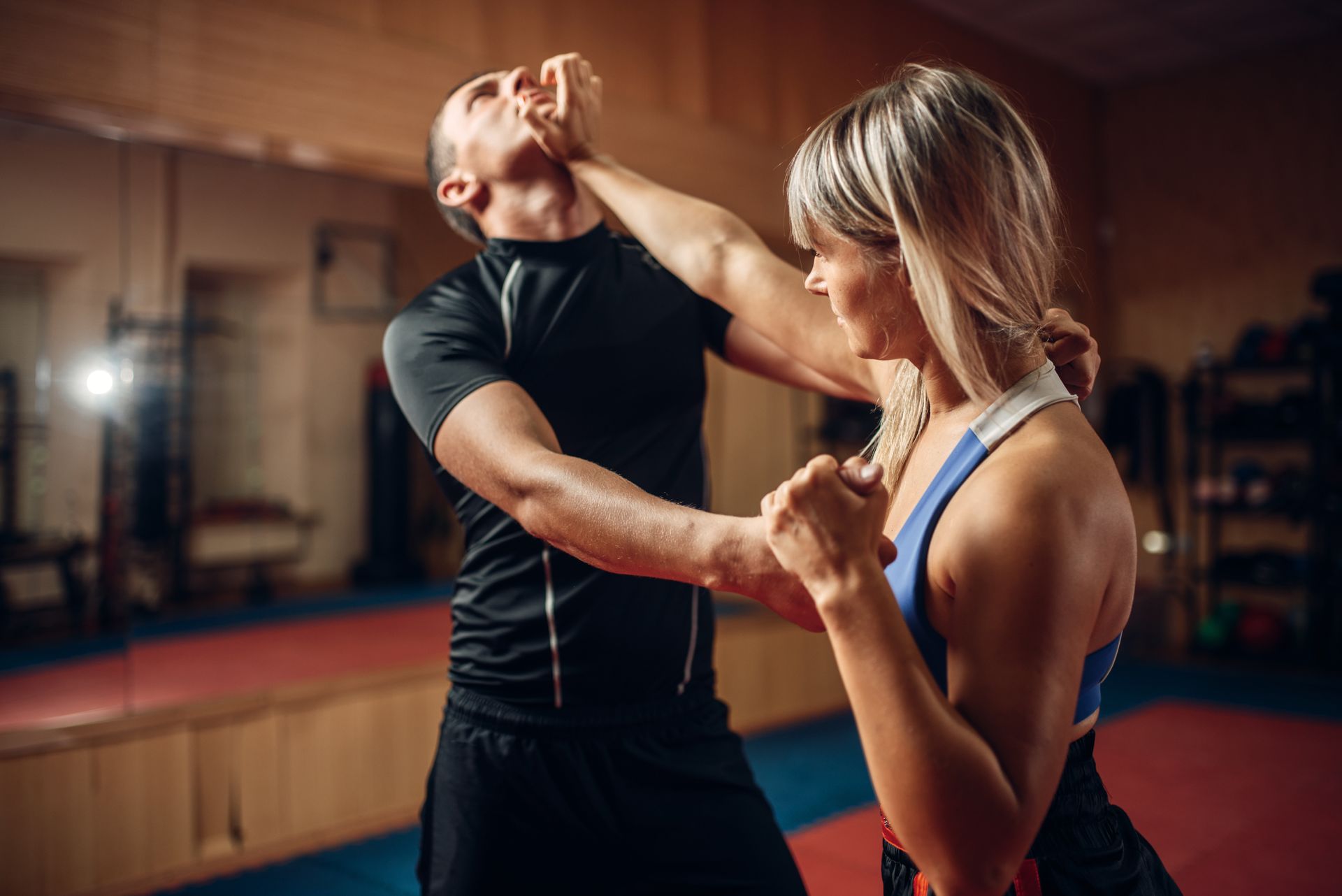 A man and a woman are practicing self defense in a gym.