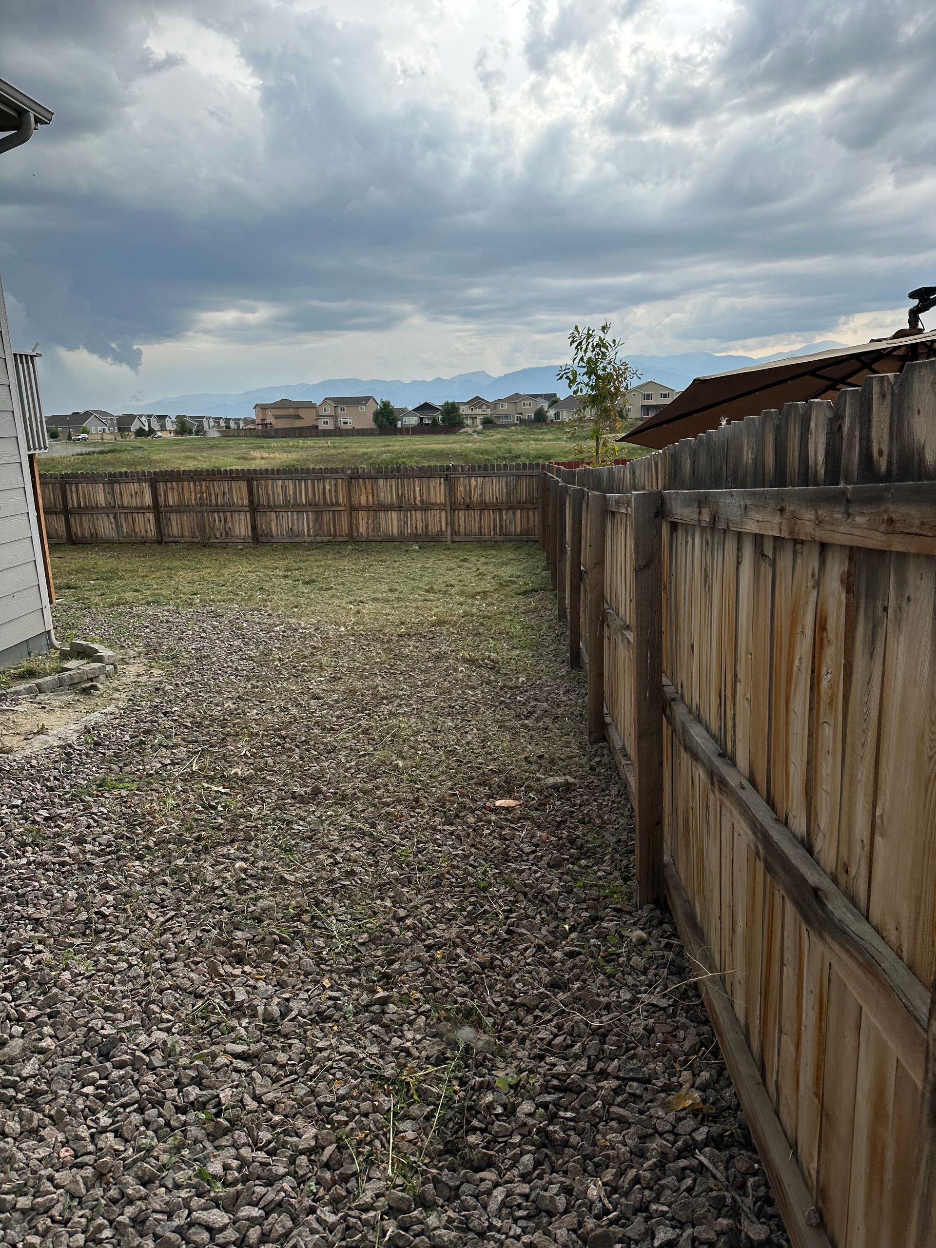 Gravel yard with wooden fence under cloudy sky, homes in background.