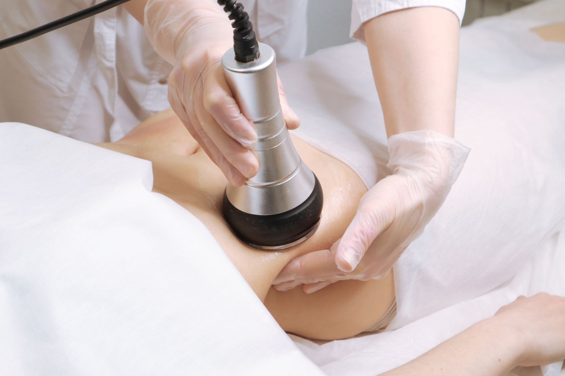 Gloved hands using a handheld device on a person’s abdomen in a clinical setting Gloved hands using a handheld device on a person’s abdomen in a clinical setting