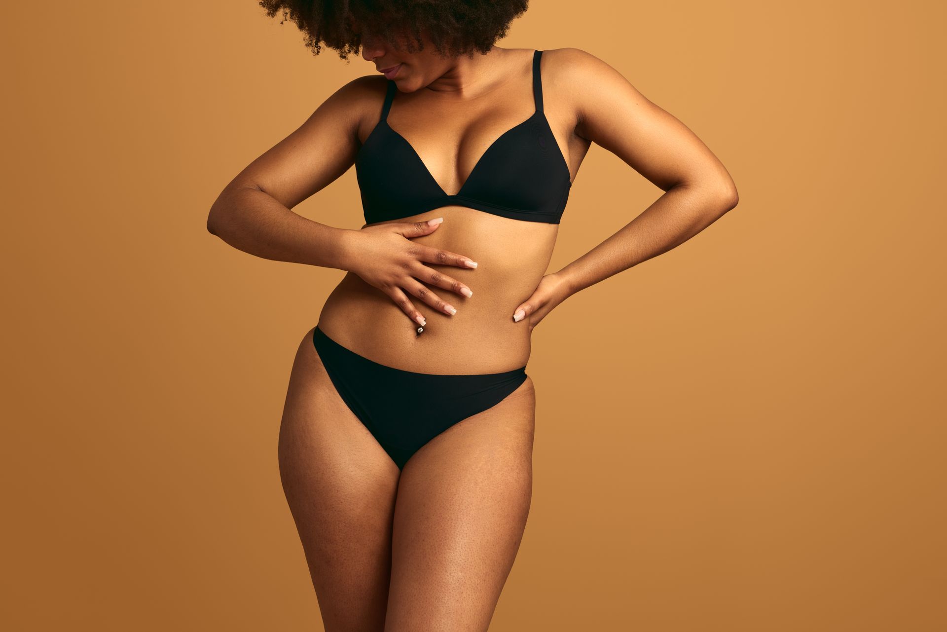 Woman in black bikini posing against a warm brown background. Woman in black bikini posing against a warm brown background.