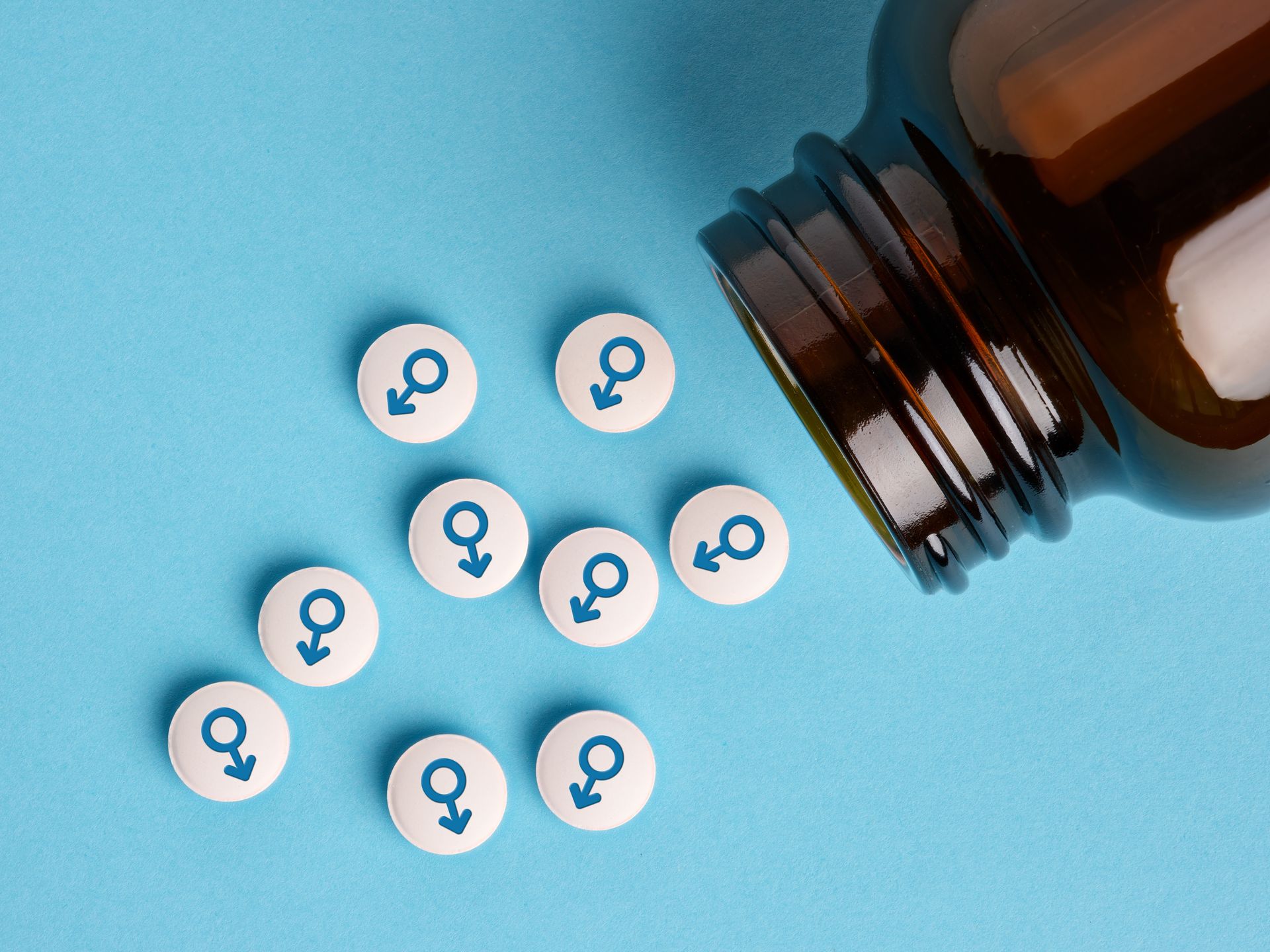 Spilled pills with female symbols beside an open amber bottle on a blue background
