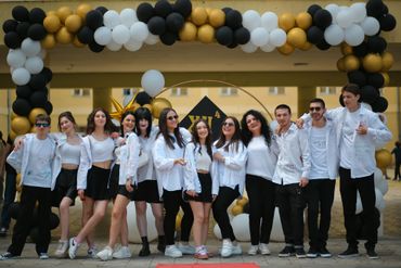 Group of people in white shirts and black bottoms posing under a balloon arch.