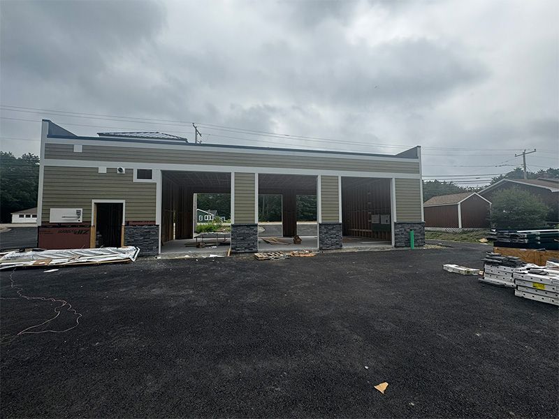 Exterior of a building under construction with multiple open bays, asphalt parking lot, and cloudy sky.