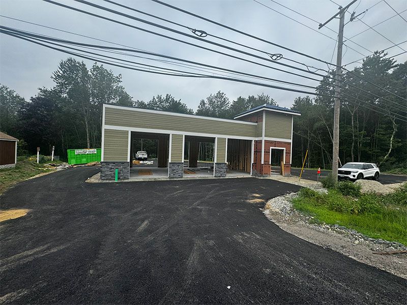 Driveway leading to a car wash building under construction with green siding and a tower. Cloudy sky.