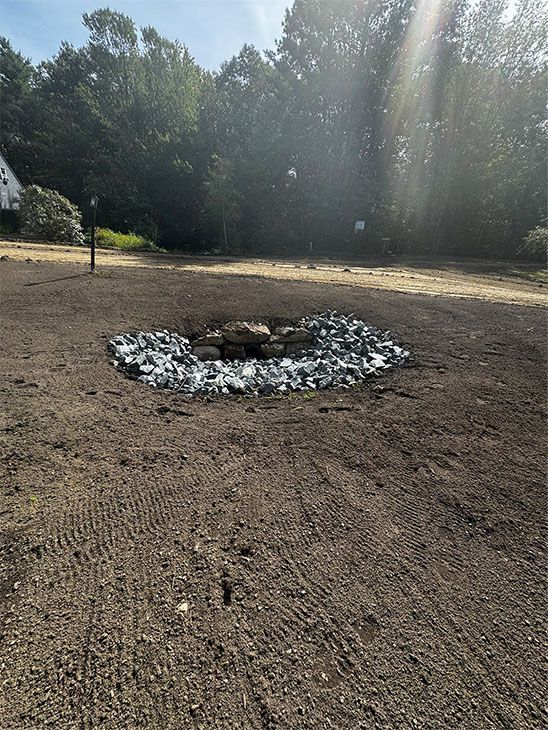 Circular rock-lined fire pit in a cleared dirt area with trees in the background.