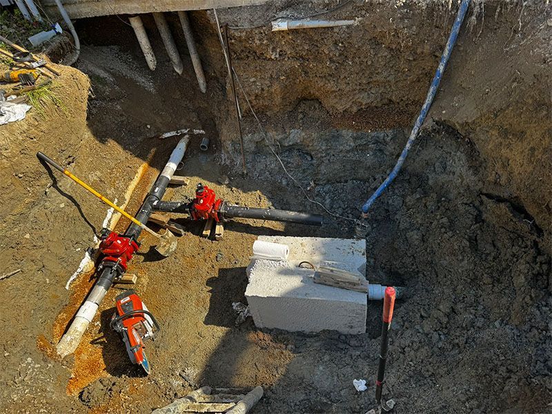 Excavation with tools around a concrete block, pipes, and soil. Red saws and picks are visible.