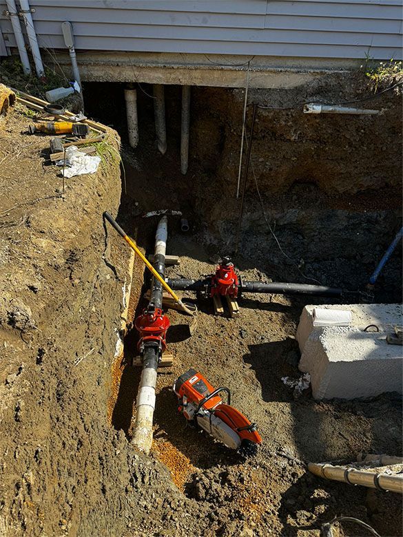 Excavated area with plumbing pipes and tools, next to a building's foundation.