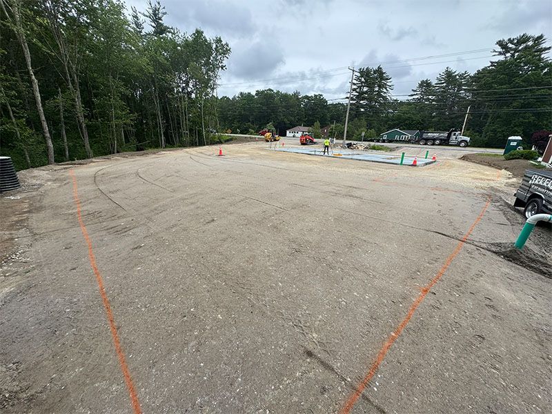 Construction site; cleared gravel lot with orange lines, trees, and construction equipment.