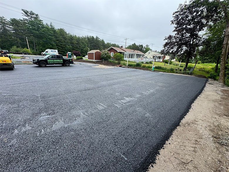 New asphalt parking lot with construction vehicle and houses in the background on an overcast day.