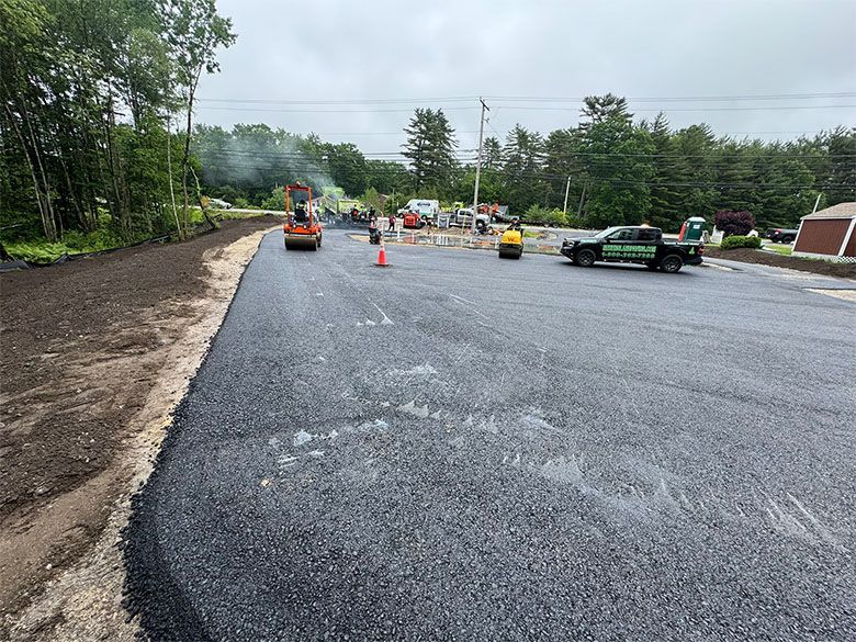 Asphalt paving in progress on a road. Workers, machinery, and a truck are present.