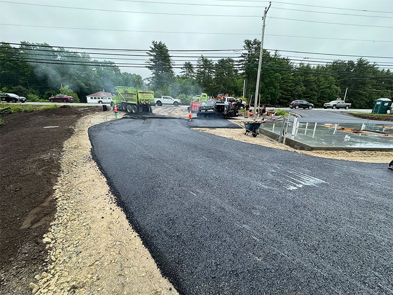 Road construction: Asphalt being laid on a roadway with construction vehicles and workers present. Cloudy sky overhead.