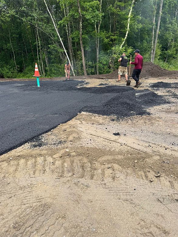 Asphalt paving with workers, cone, and trees in the background.