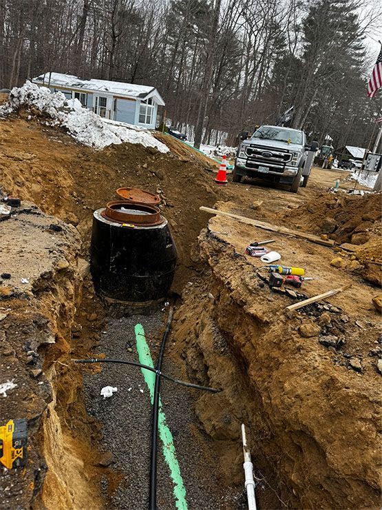 A septic tank installation. A black tank sits in a trench with pipes; a pickup truck parked nearby. Snow on the ground.