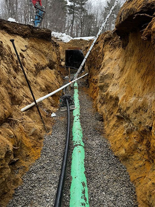 Construction of a trench. Green pipe, black cable, gravel bed, and brown soil.
