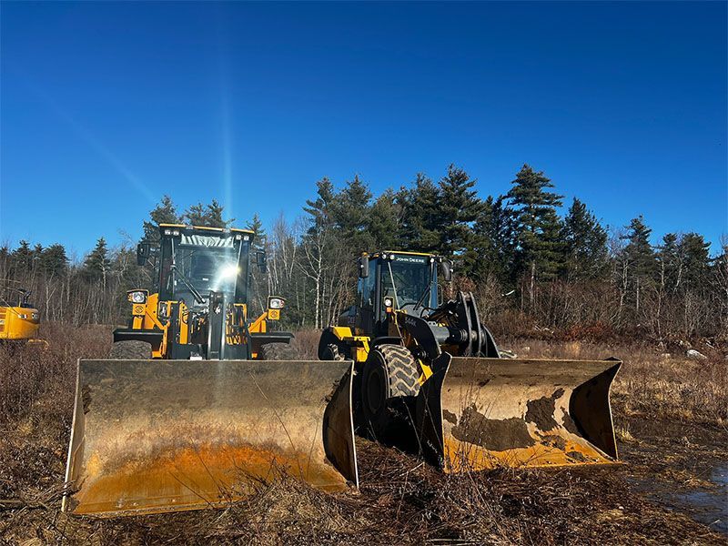 Two yellow bulldozers with blades up, parked in a clearing under a blue sky.