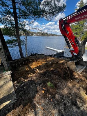 Red excavator digging near a lake, partially obscuring the water view with trees in the background.
