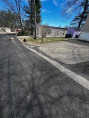 Asphalt road leading to gravel parking area near a weathered building with purple trim under a bright blue sky.