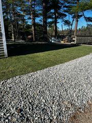 Gravel path beside a lawn; tall trees and building in the background. Bright blue sky.