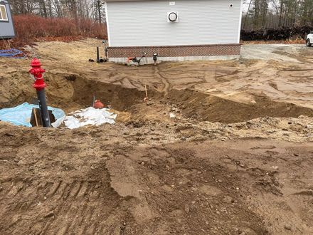 Excavation site with red fire hydrant, utility lines, and a light-colored building in the background.