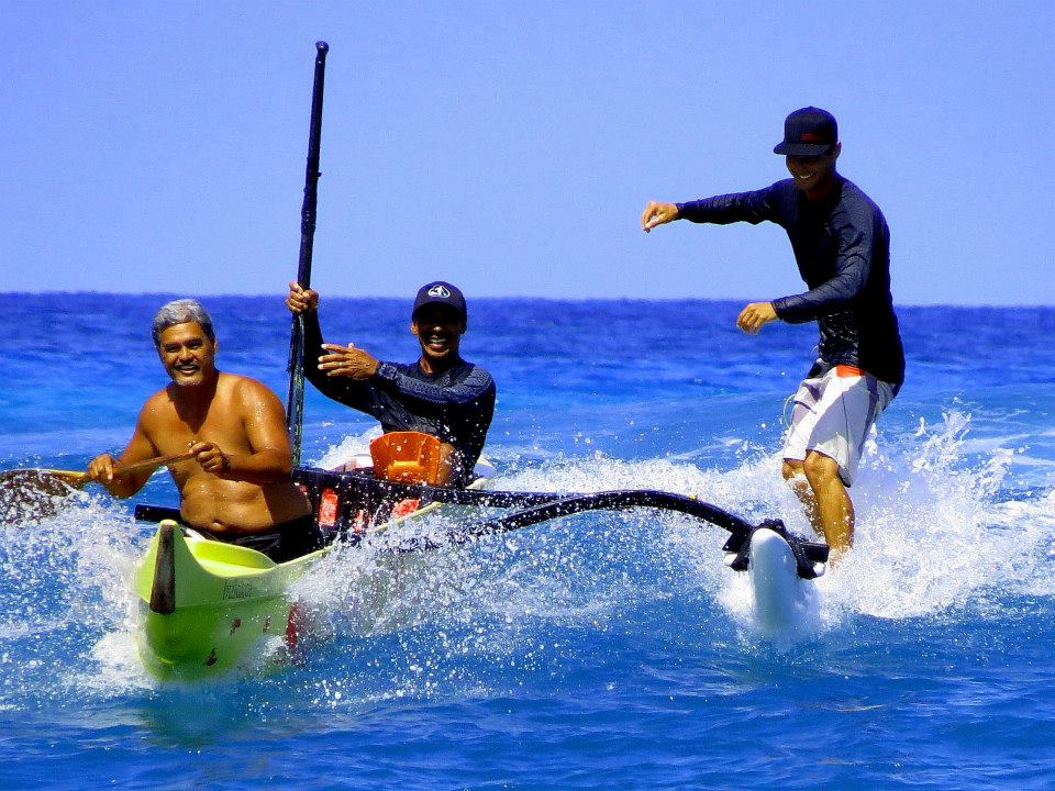 Three men are riding a surfboard in the ocean