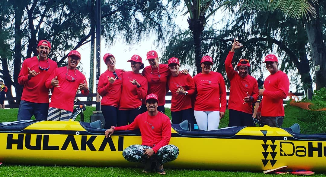 A group of people in red shirts are posing for a picture in front of a yellow boat.