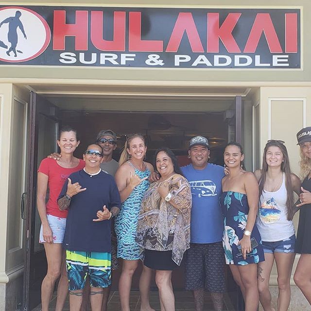 A group of people standing in front of a hulakai surf and paddle sign