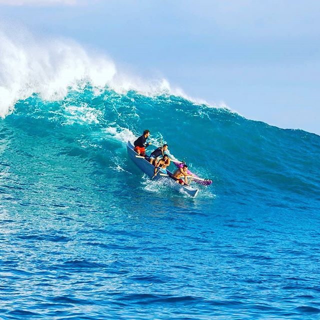 A group of people are riding a wave on a surfboard in the ocean.