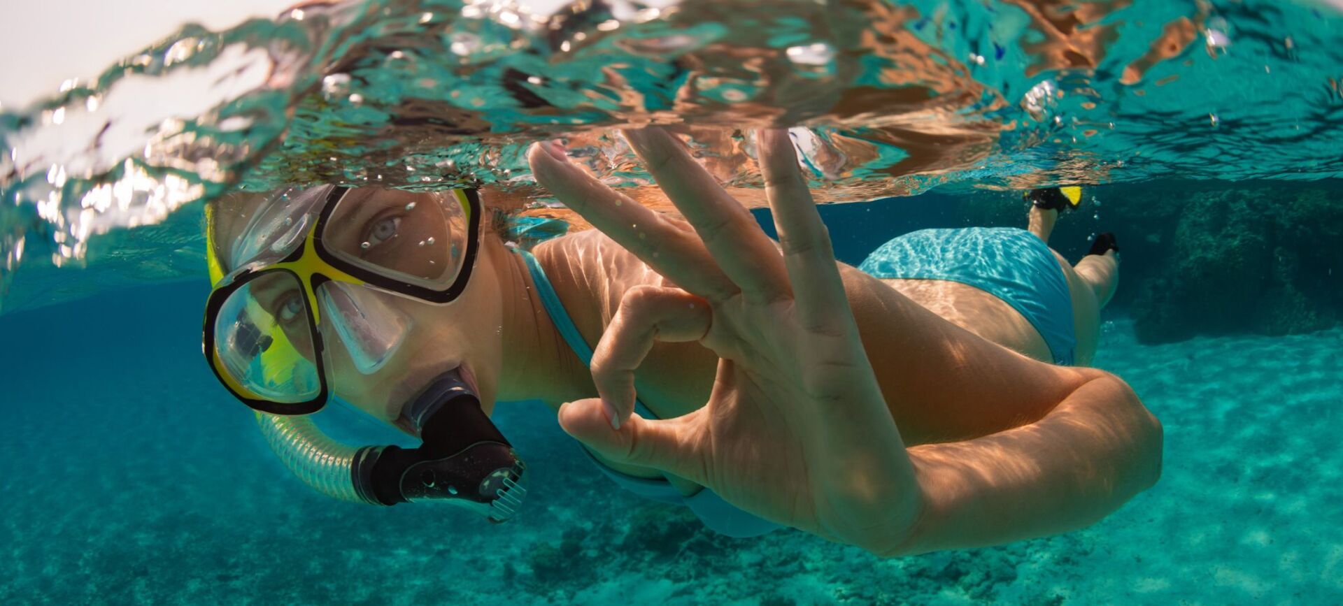 A woman is snorkeling in the ocean and giving the ok sign.