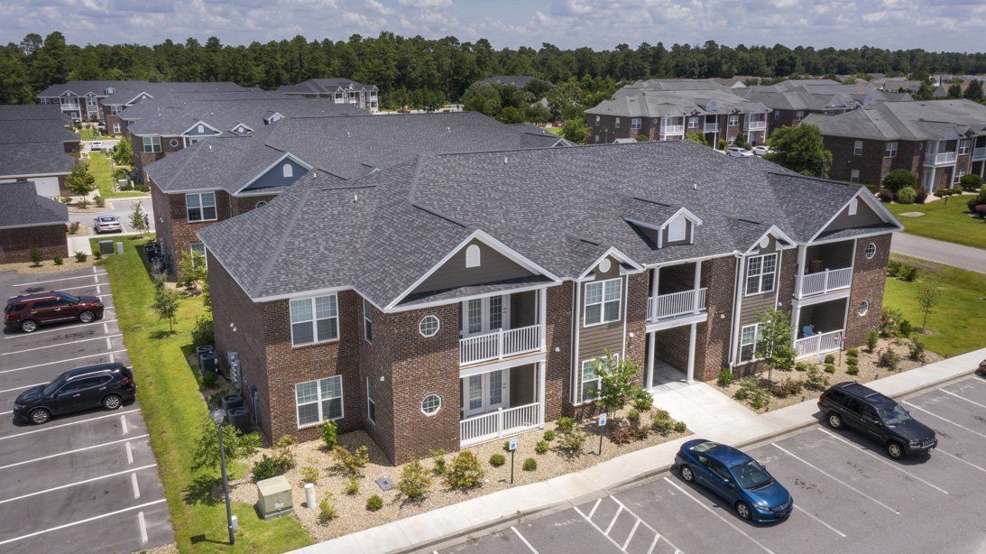 An aerial view of a brick apartment building with cars parked in front of it | Cloisters at Carolina Forest