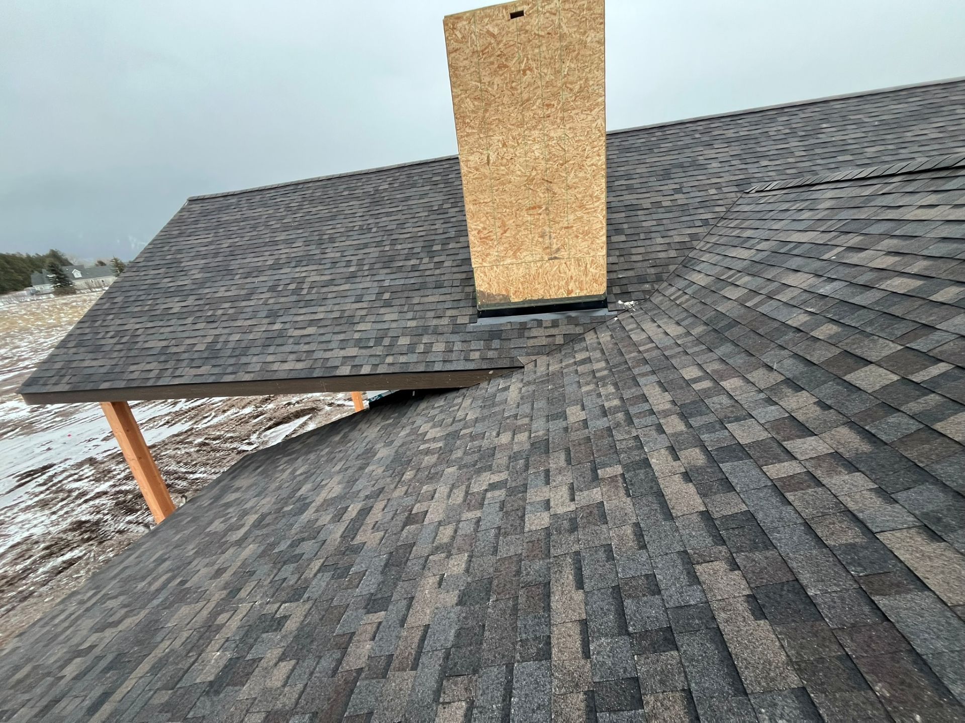 Roof with dark gray shingles and a central chimney, viewed from above.