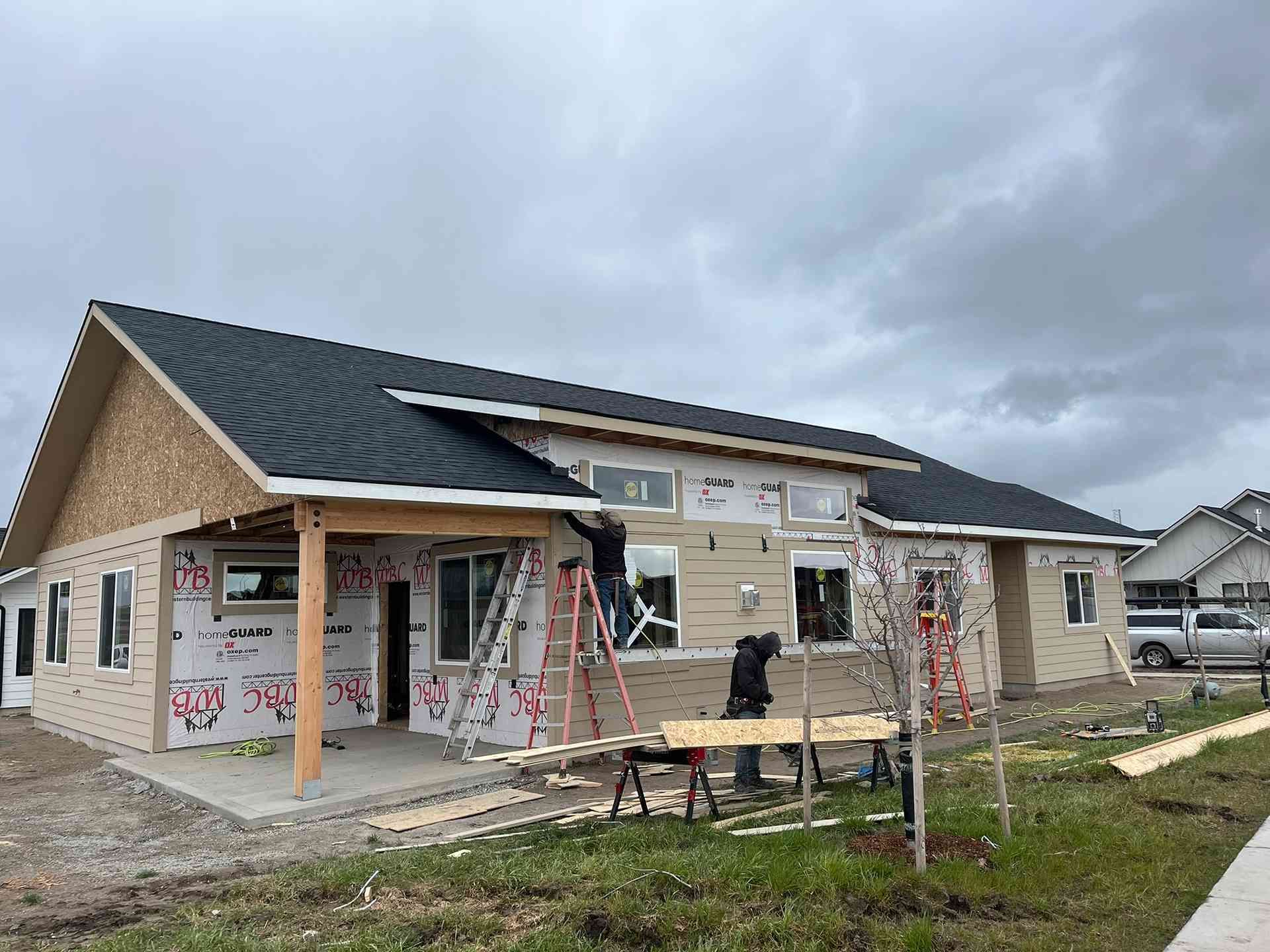 Partially built single-story house with workers, construction materials, and cloudy sky overhead