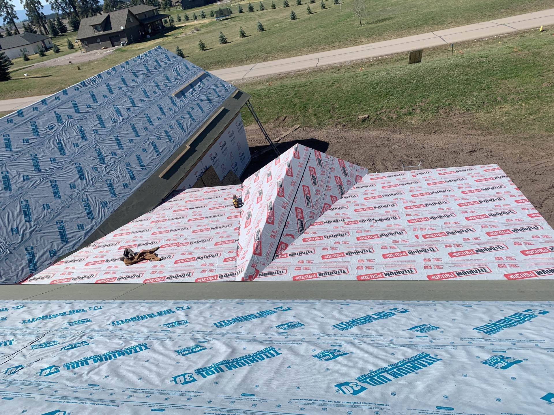 Roofing materials stacked on a rooftop with a grassy field in the background.